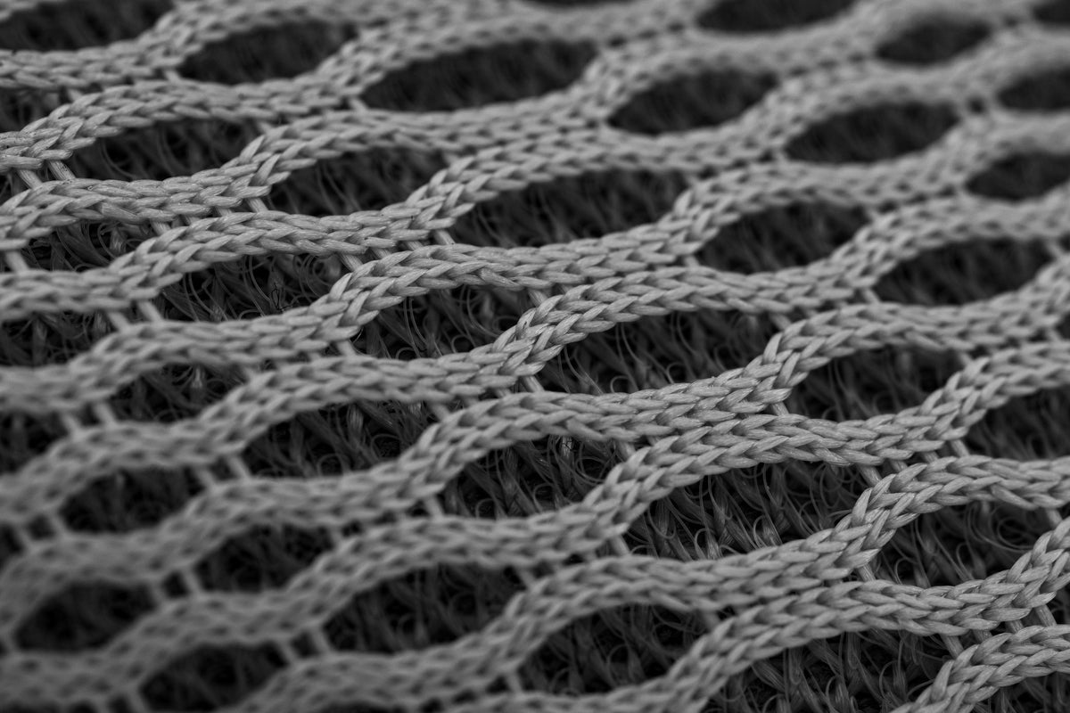 A detailed close-up of a grey knit nylon fabric creating an abstract geometric pattern.