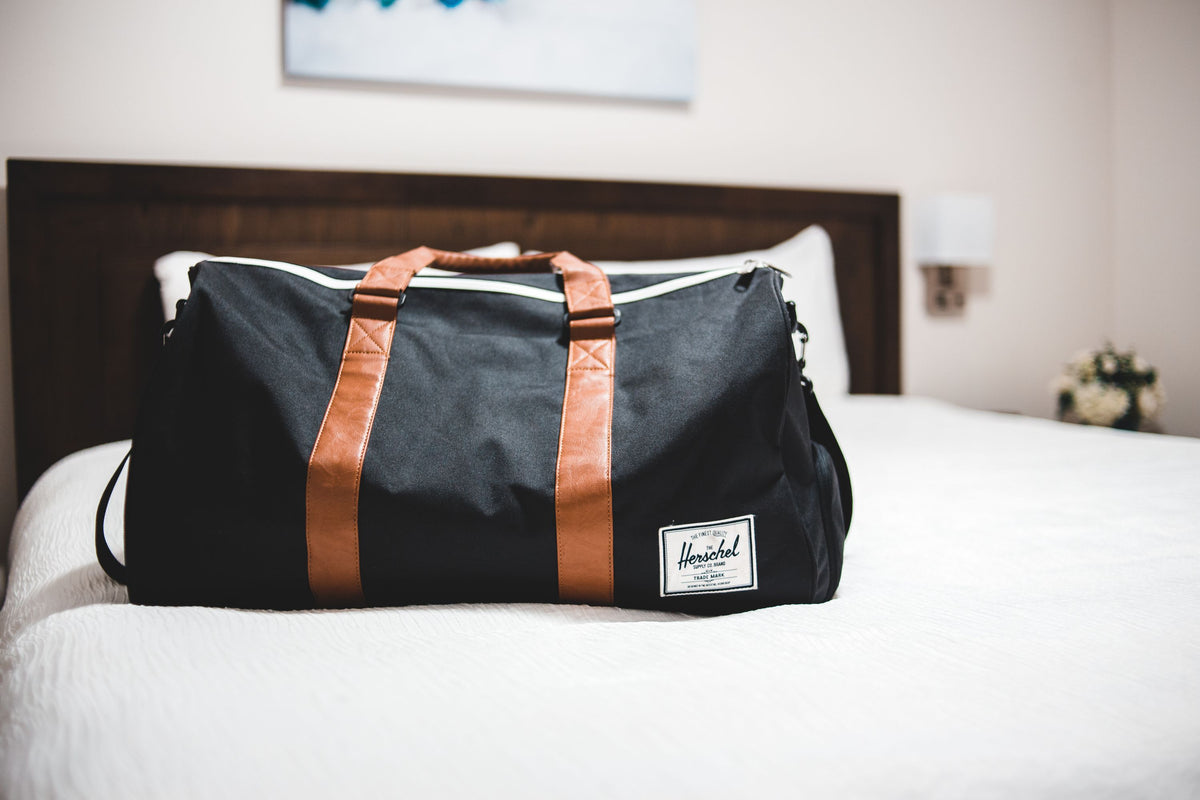 Contemporary baggage bag with inscription on white bed cover in light hotel room